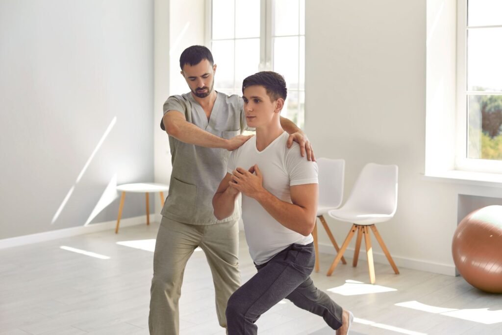 Male physiotherapist assists a patient performing a lunge in a bright clinic, showcasing physiotherapy services in Thailand.