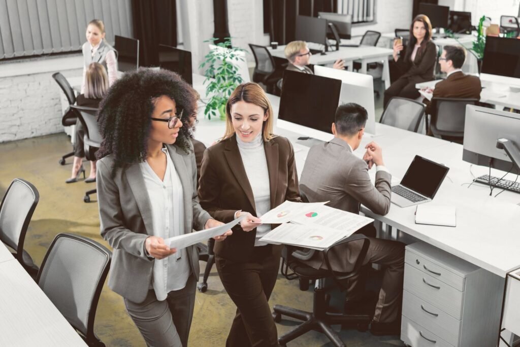 Two businesswomen analyze conversion rate audit reports with charts in a modern office, boosting ROI.