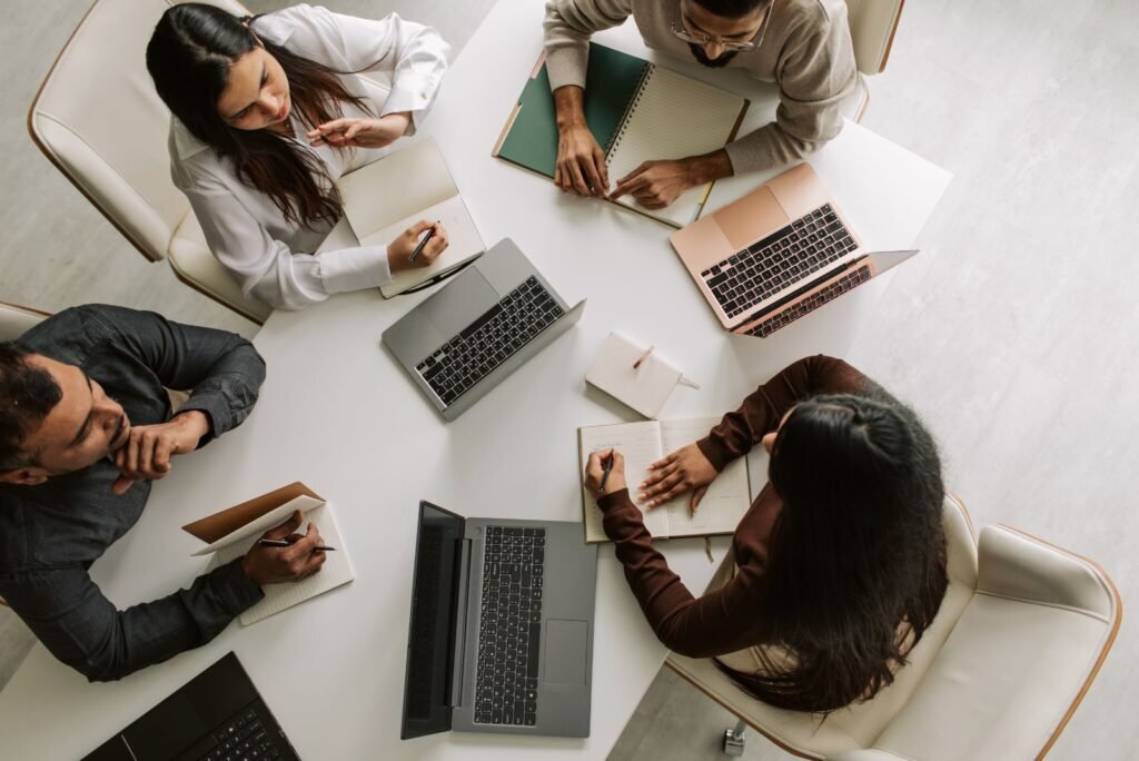 Overhead view of four professionals collaborating on online reputation strategies at a table with laptops and notebooks.