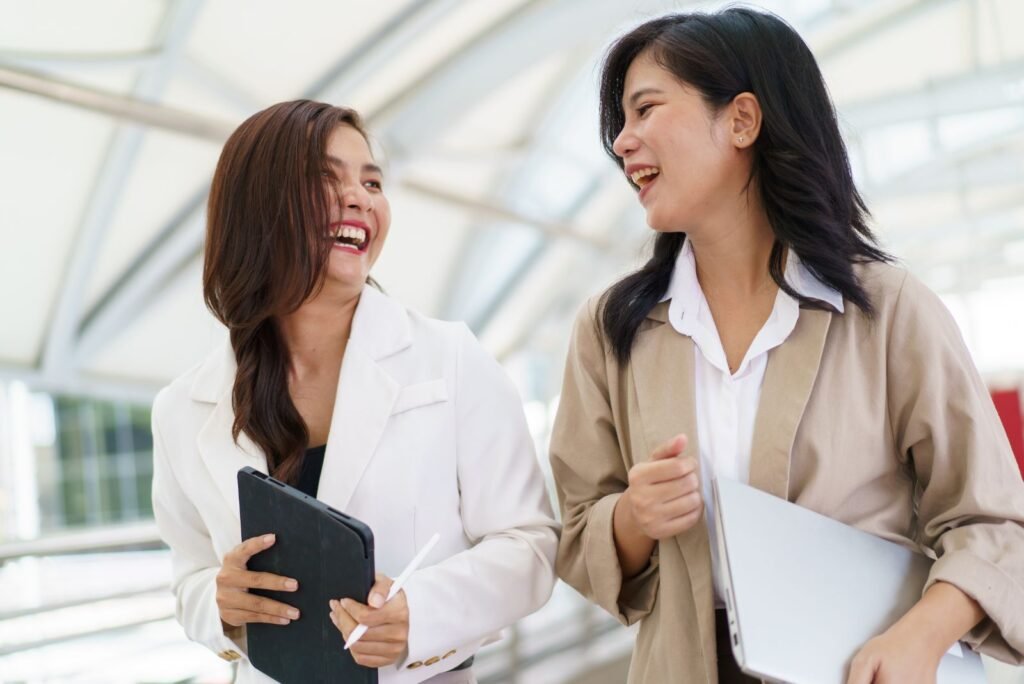 Happy businesswomen with tablet & laptop, collaborating on strategies to boost online reputation and trust.