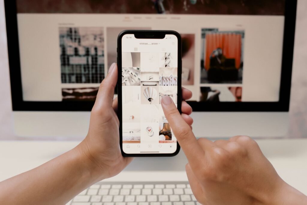 Hands interact with a smartphone displaying content, a desktop website visible behind, emphasizing continuous website management.