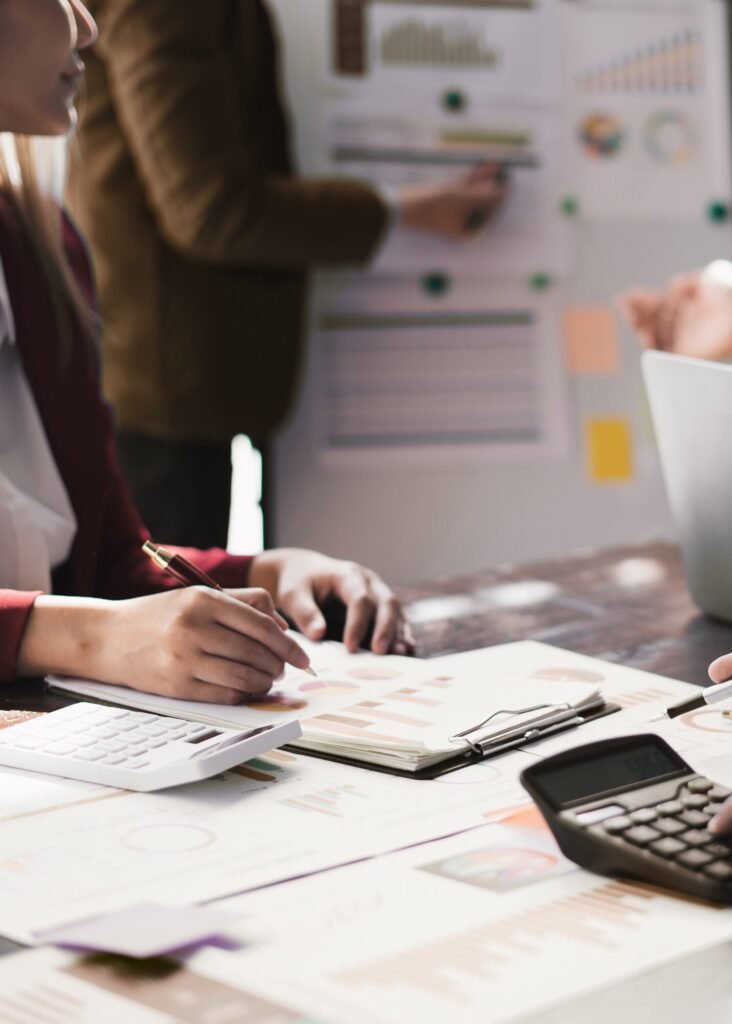 Business experts review Google Ads campaign performance data, using charts, calculators, and a whiteboard for strategic planning.