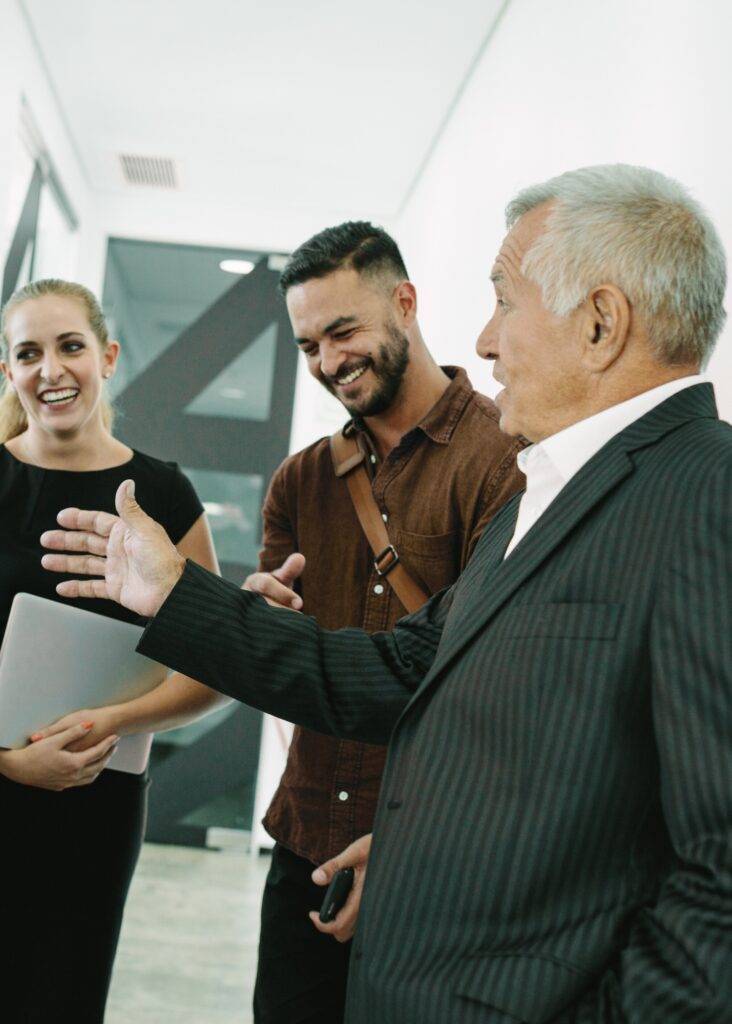 Three smiling LinkedIn ad agency professionals, including a gesturing senior, collaborating on strategy in an office.