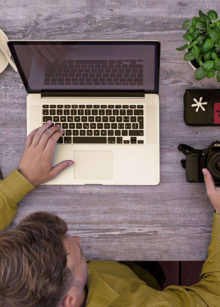Creative professional working on a laptop, holding a DSLR camera, for expert YouTube video ad campaigns.