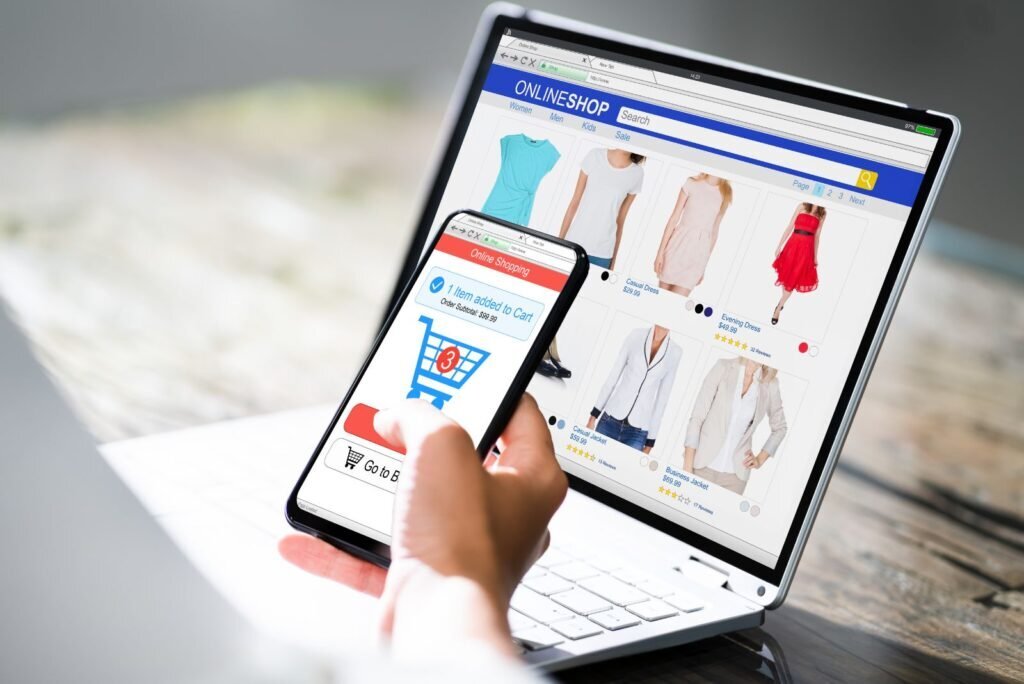 Hand holding phone with 'item added to cart' notification, laptop displays online clothing store. Drives e-commerce conversions.