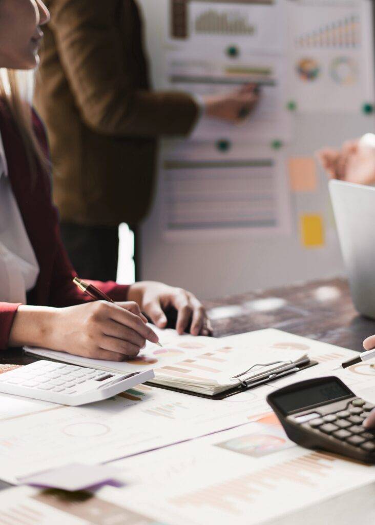 Business experts review Google Ads campaign performance data, using charts, calculators, and a whiteboard for strategic planning.