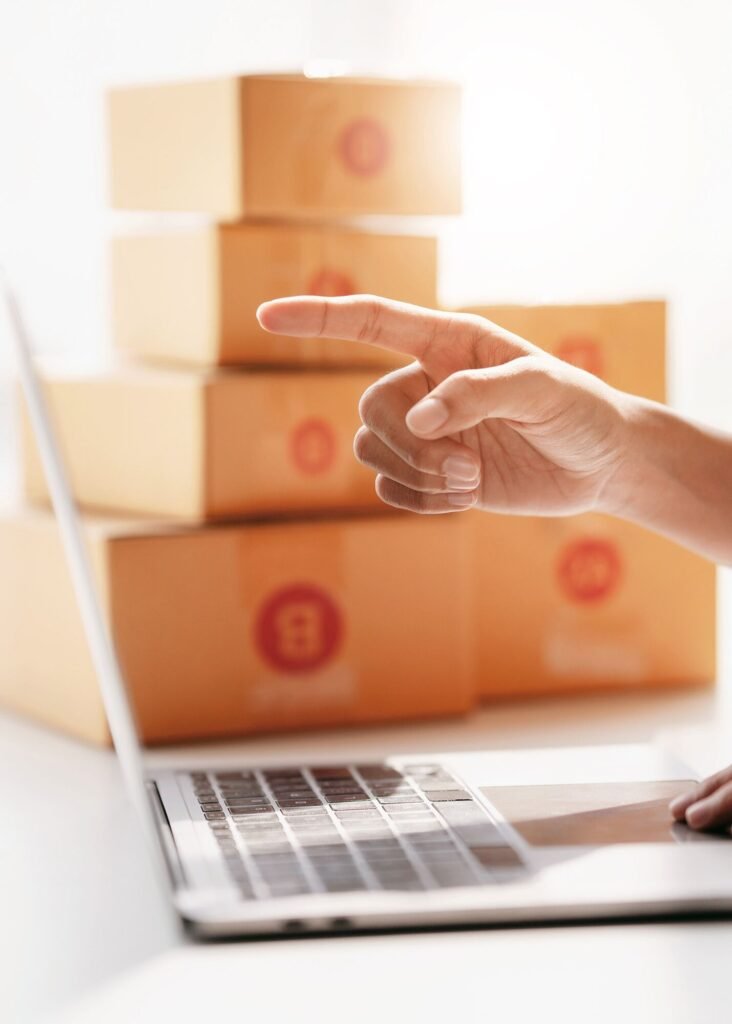 Hand pointing at stacked e-commerce shipping boxes beside a laptop, representing digital marketing for sales growth.
