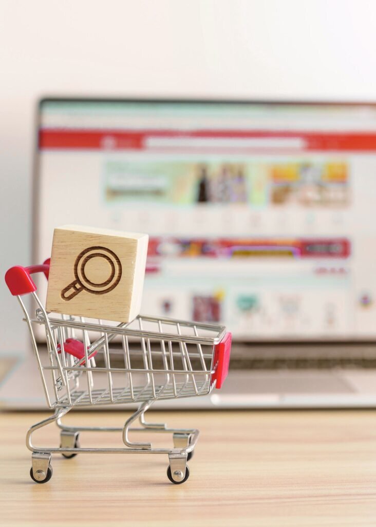Miniature shopping cart, search icon block, and e-commerce site on laptop. Expert digital marketing finds customers, drives sales & ROAS.