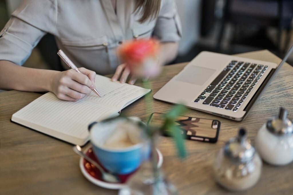 Hands writing content strategy in a notebook beside a laptop, symbolizing thoughtful content marketing and SEO article creation.