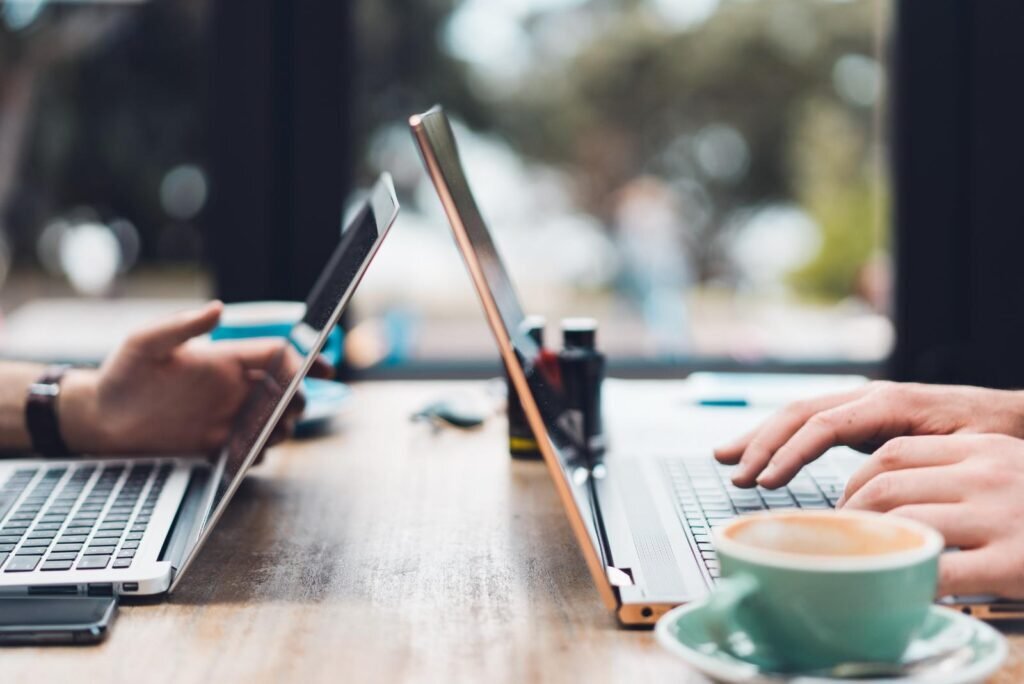 Hands typing on laptops with coffee, representing engaged users online for effective Facebook remarketing campaigns.