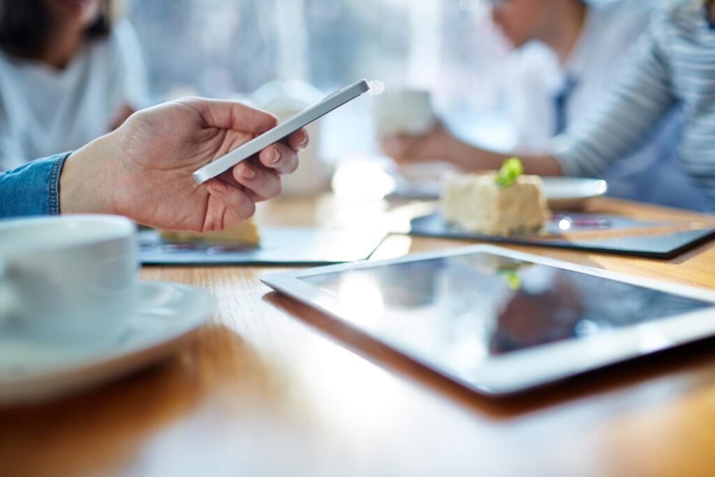 Close-up of a hand using a smartphone, with a tablet and coffee, representing users engaged by Facebook remarketing.
