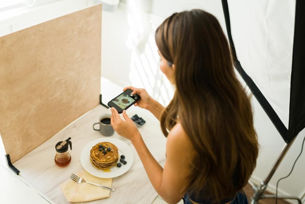 Woman photographing delicious pancakes with a phone, creating engaging content for Facebook remarketing campaigns.