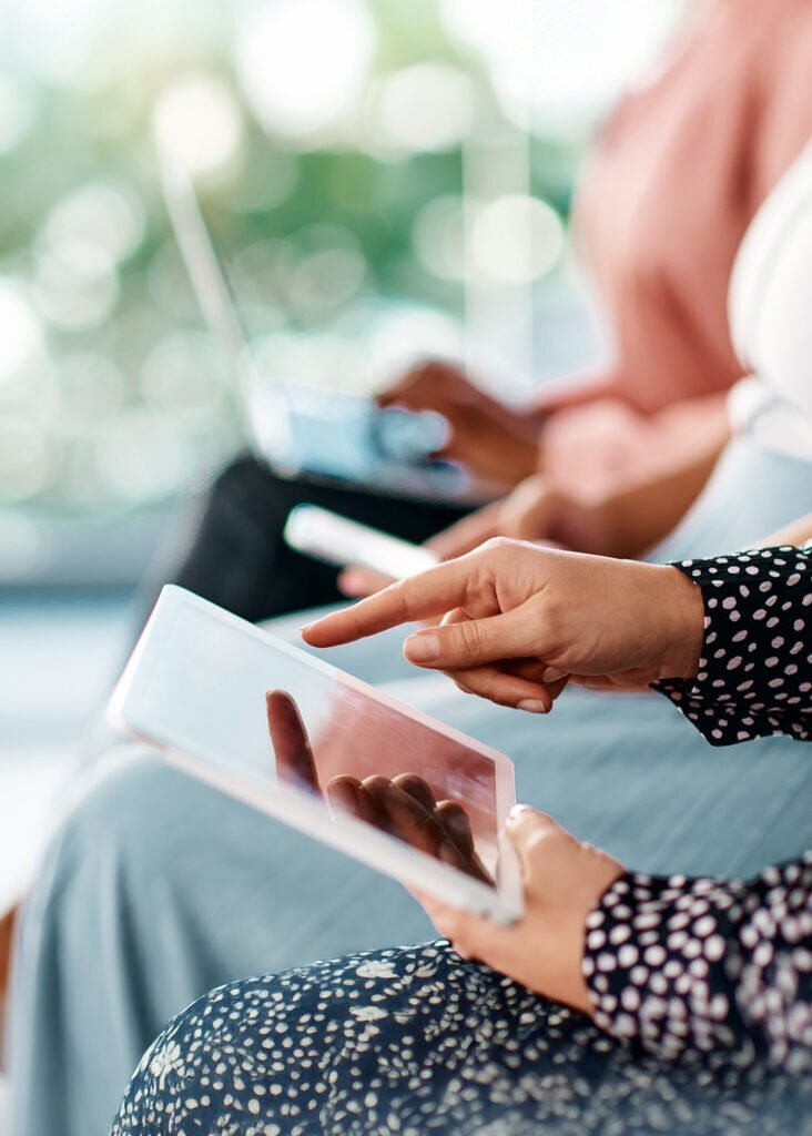 Hands tapping a tablet screen, with a blurred laptop in the background, showcasing diverse PPC advertising platforms.