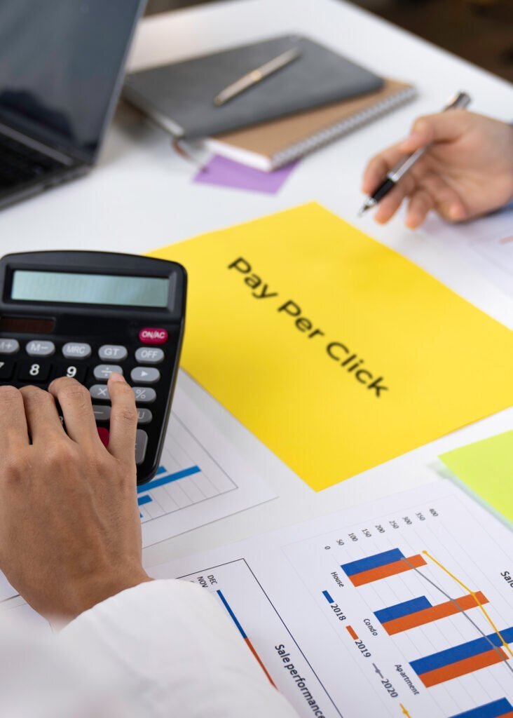 Expert analyzing PPC campaign performance with a calculator, charts, and a "Pay Per Click" document to maximize advertising ROI.