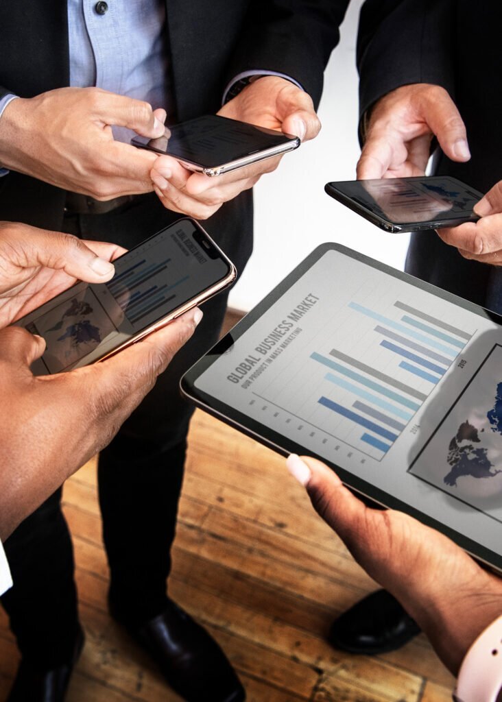 Business team analyzing global market data on phones and a tablet for optimal PPC advertising ROI.