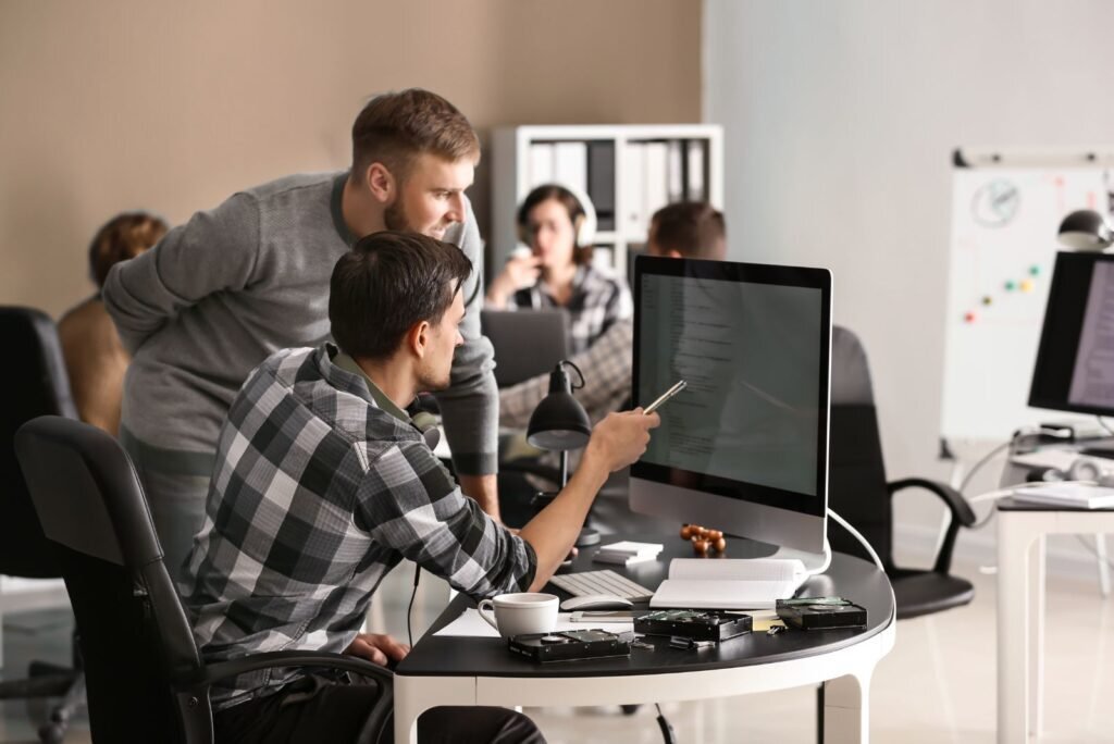 Two SEO specialists analyze website structure on a monitor, strategizing keyword mapping for improved search ranking.