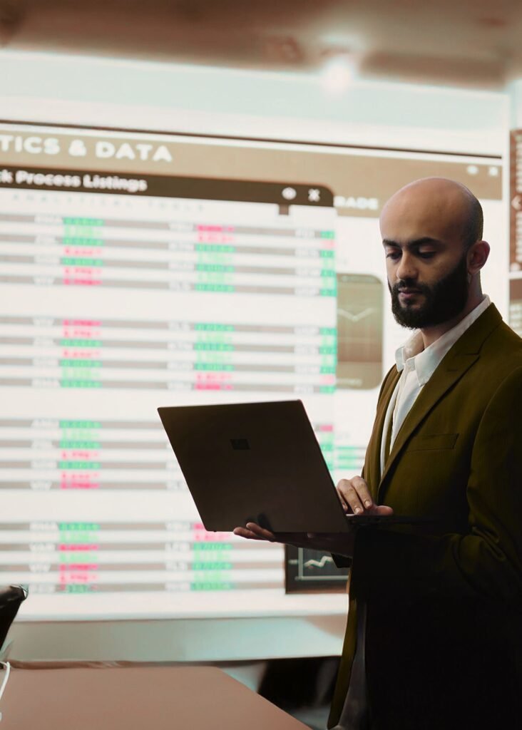 Professional analyzing programmatic advertising data on a laptop, with performance metrics displayed on a large screen, highlighting real-time optimization.