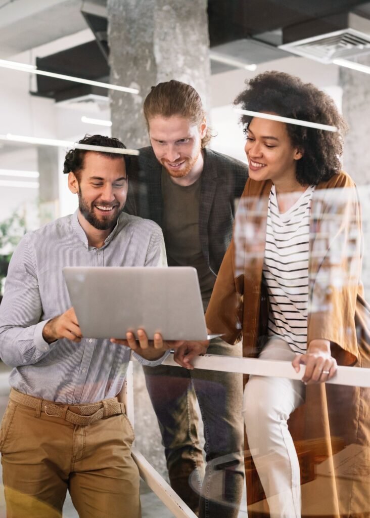 Diverse team of three professionals collaborating and smiling while reviewing data on a laptop for programmatic advertising.