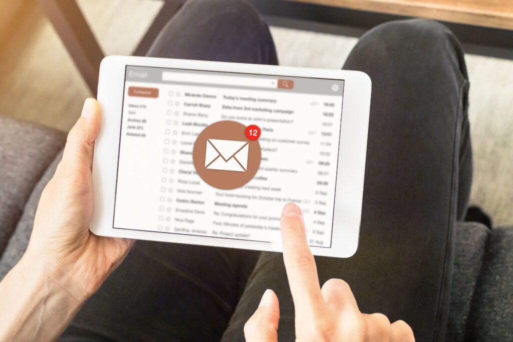 Hand tapping a tablet screen showing an email inbox with 12 new messages, illustrating successful Bangkok email marketing campaigns.