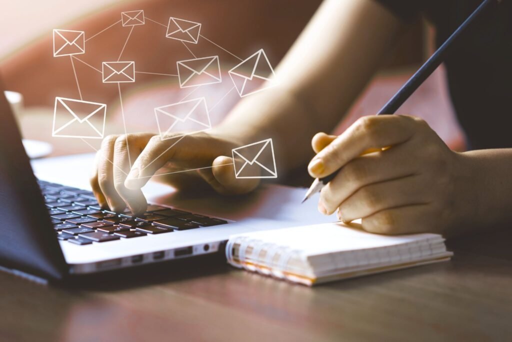 Hands typing on a laptop and writing notes, surrounded by digital email icons, illustrating email campaign management services.