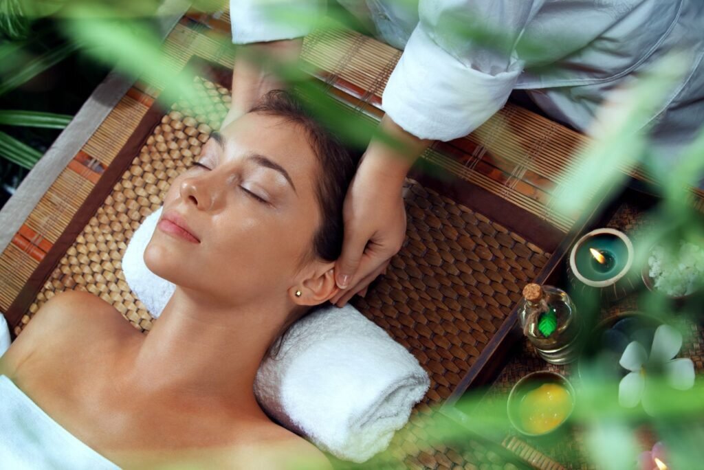 Relaxed woman with closed eyes receiving a soothing head massage at a tranquil spa, surrounded by oils and candles.