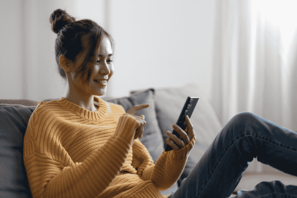 Smiling woman on a couch points at her smartphone, illustrating engaging Google Display Ad creative driving results.