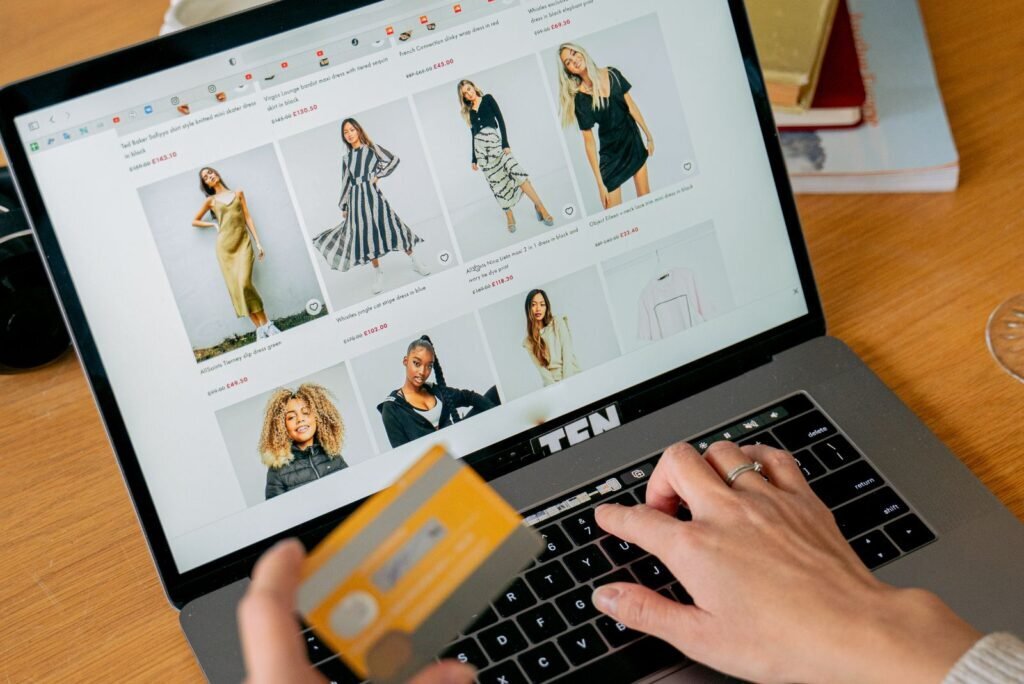 Customer's hands browsing clothing on a laptop, holding a credit card to complete a Google Shopping ad purchase.