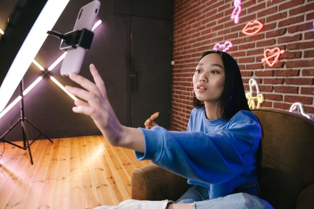 Focused young woman creating scroll-stopping TikTok video content on a smartphone, bright lights, and trendy neon signs.