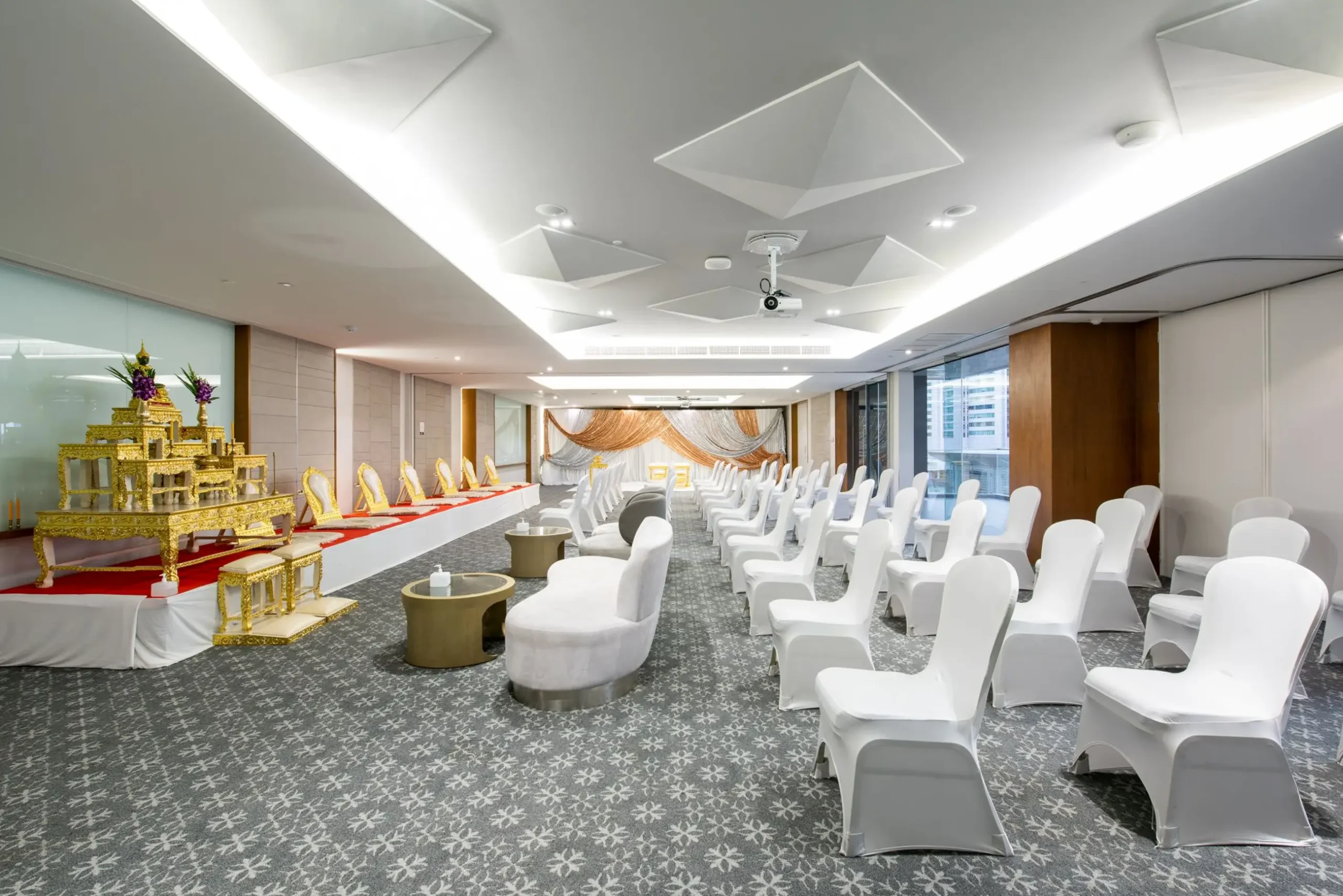 Spacious hotel event room in Thailand, featuring a golden ceremonial altar and rows of white chairs for diverse hospitality events.