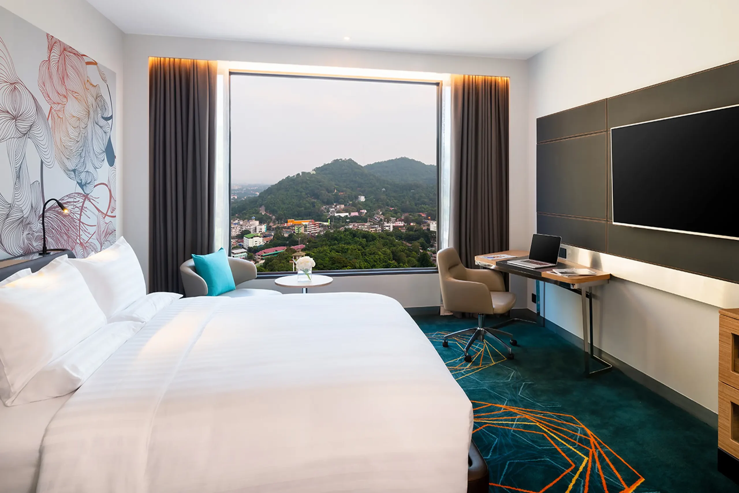 Upscale hotel room in Thailand with a comfortable bed, workspace, and scenic mountain view, ideal for hospitality marketing.