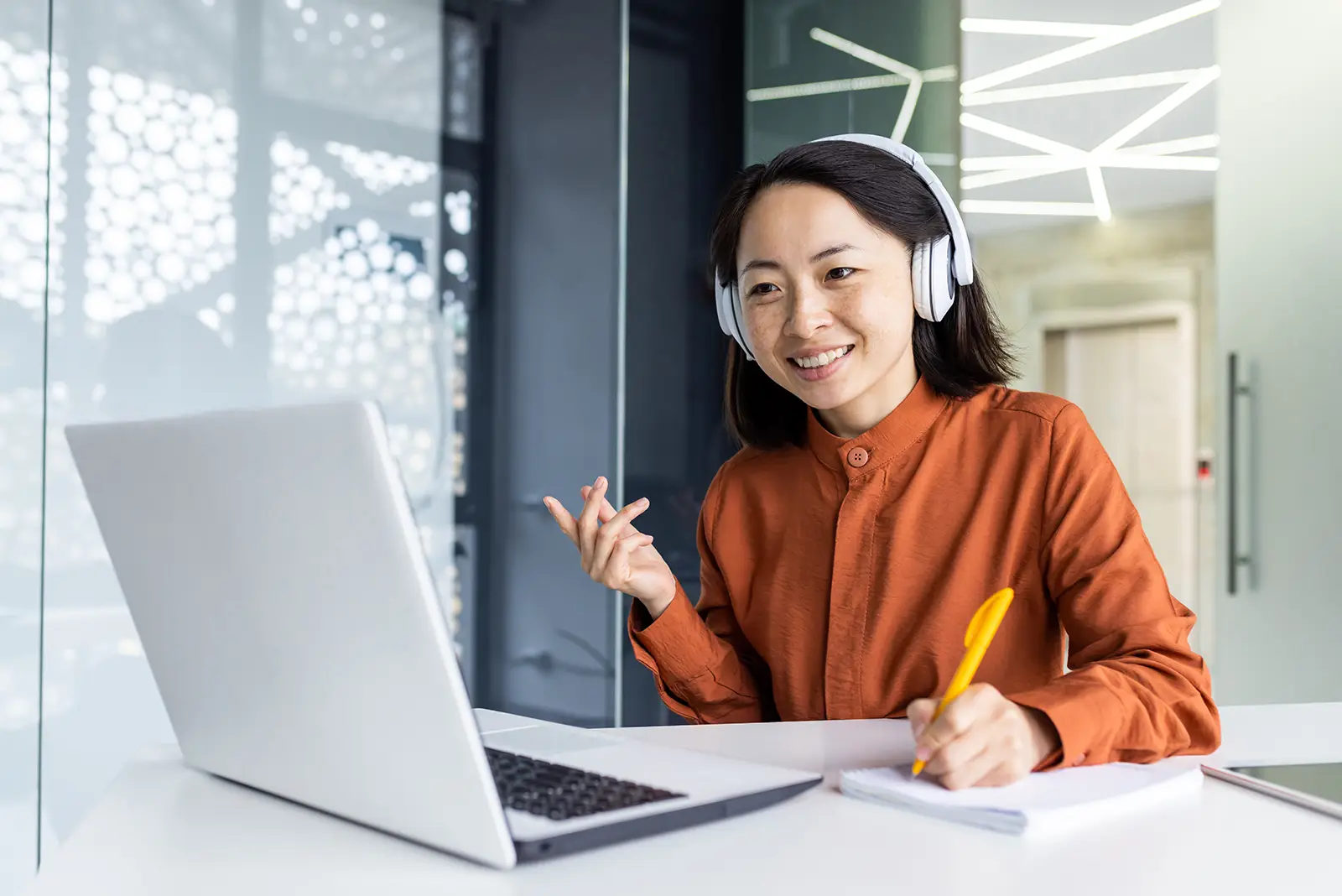 Smiling woman in headphones discussing digital marketing strategy on a laptop, taking notes for a client success case study.